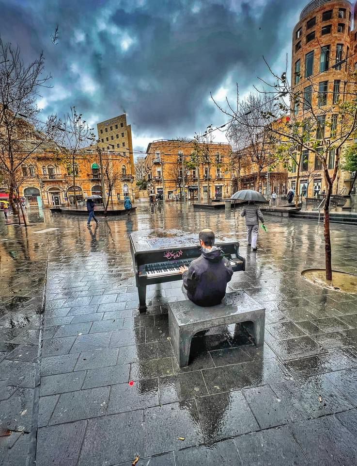 Man playing a Cadenza outdoor piano in a rainy city square