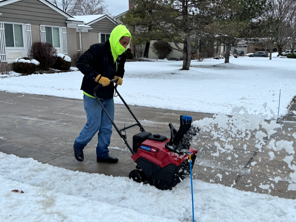 Person using a red snowblower to clear snow from a driveway.