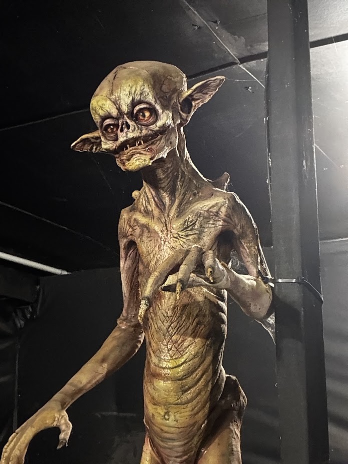 Tall animatronic alien creature prop with glowing yellow-orange eyes and leathery skin
