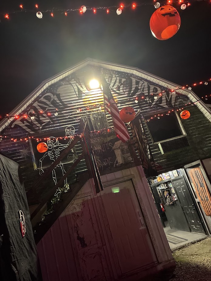 Exterior of Fear on the Farm haunted attraction at night with red string lights, jack-o-lanterns, and a skeleton decoration