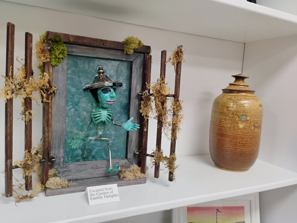 Whimsical framed sculpture and handmade pottery on a shelf