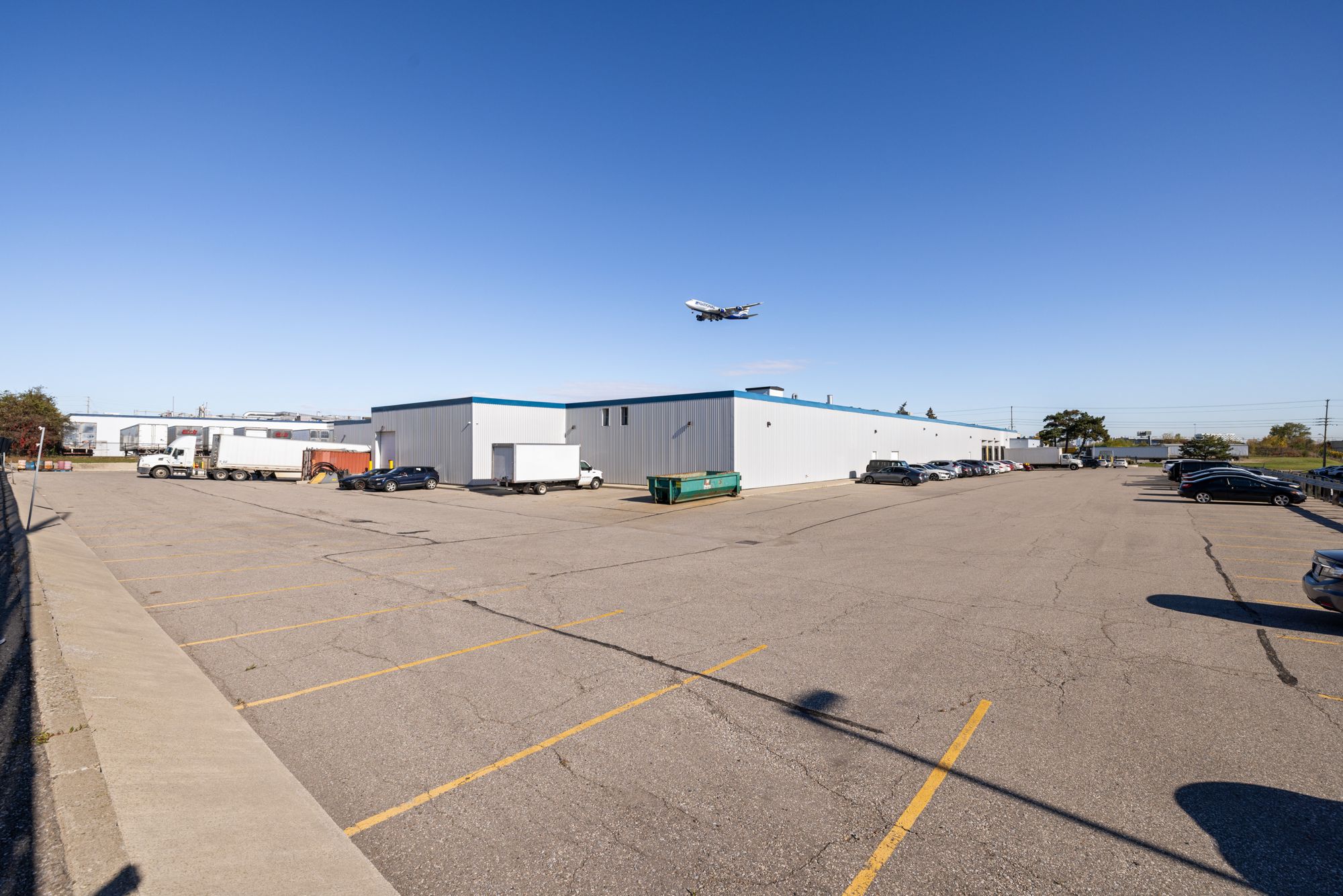 Parking and exterior at 6400 Northwest Drive in Mississauga, with an aircraft overhead on approach to Pearson Airport