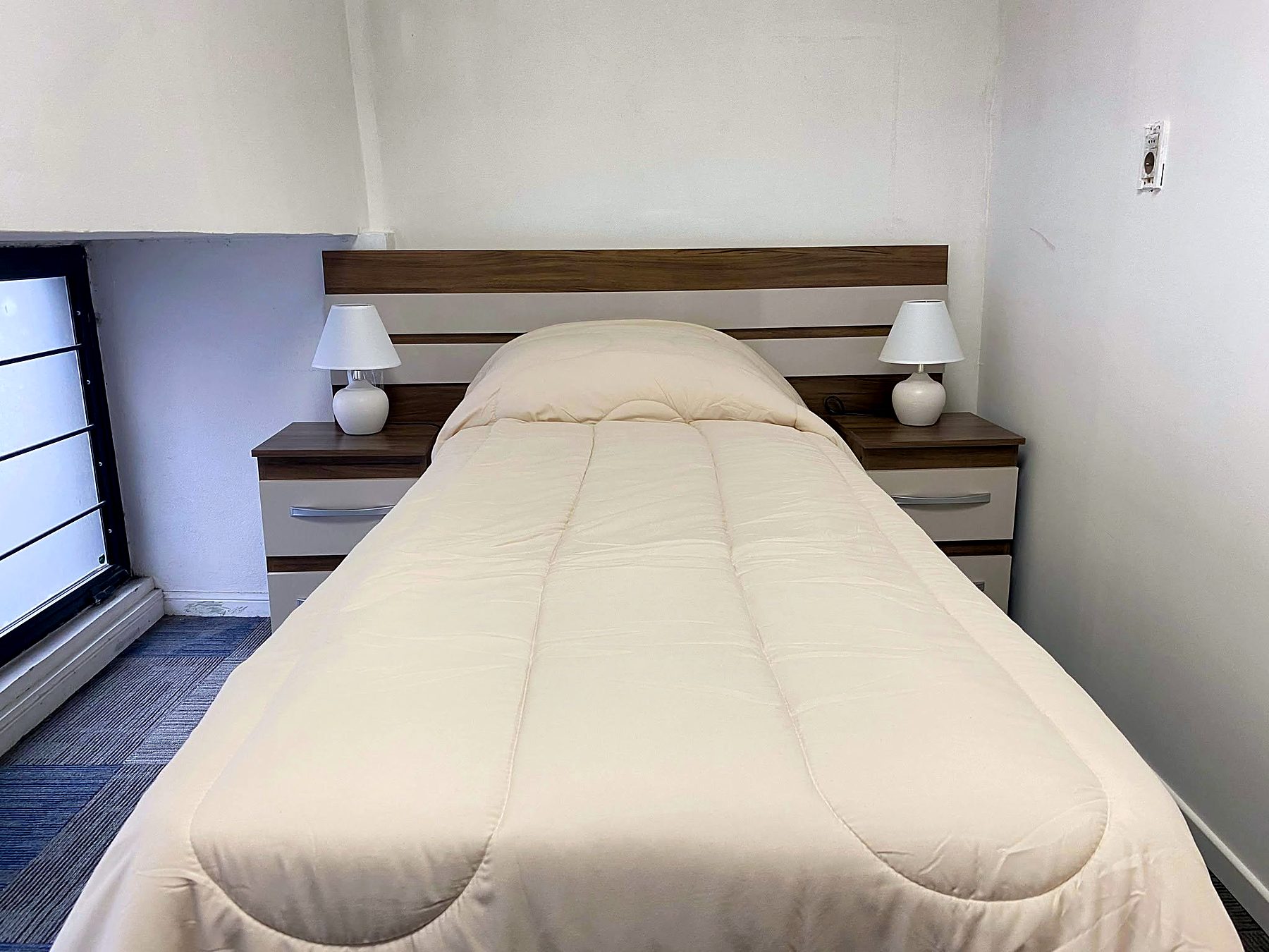 Habitación individual con cama tendida, mesas de luz y lámparas