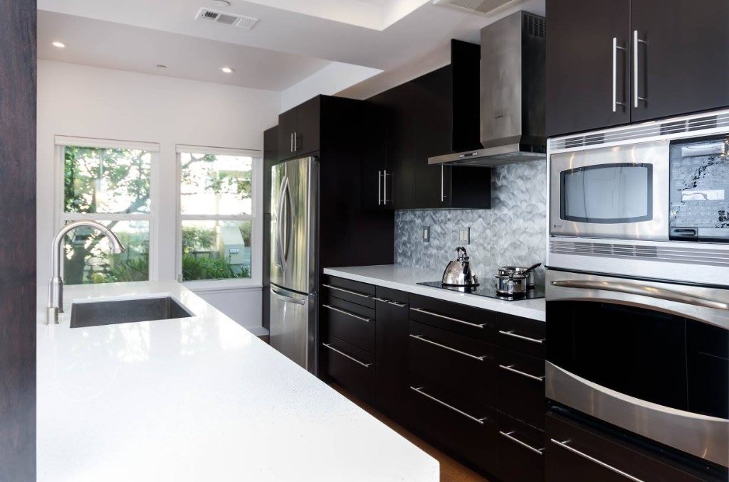 Sunnyvale kitchen with dark espresso cabinetry, white quartz countertops, a metallic backsplash, a large island, and a modern fireplace with TV niche.