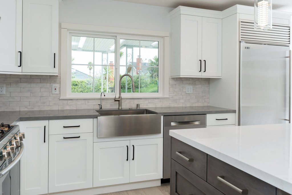 Millbrae open-concept kitchen with white shaker cabinetry, a driftwood-tone island, farmhouse sink, stainless appliances, and gray quartz countertops.