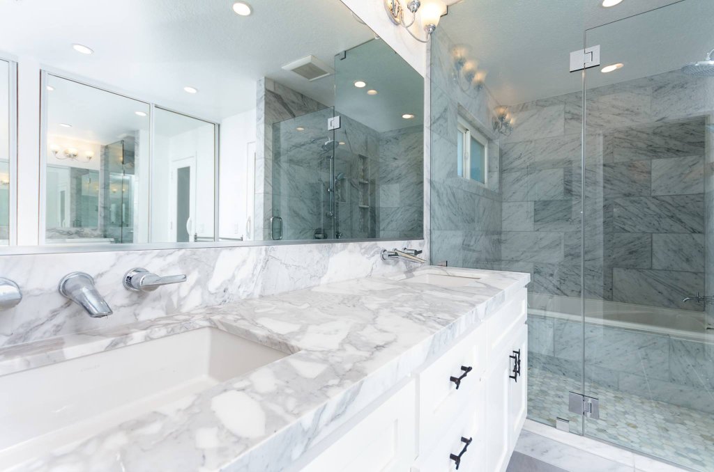Luxury master bathroom remodel featuring full Calacatta marble tile walls and floors, soaking tub with shower, double vanity with marble countertop, frameless glass