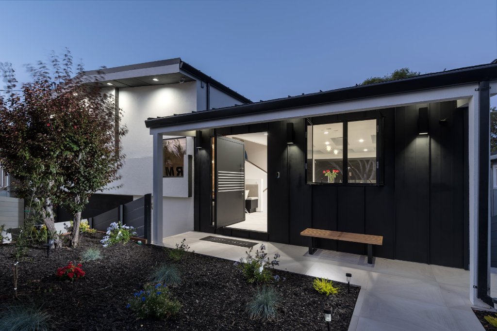 Open-concept Los Altos kitchen with matte-black flat-panel cabinetry, a Calacatta marble waterfall island, professional range, and glass-globe pendants beneath skylights.