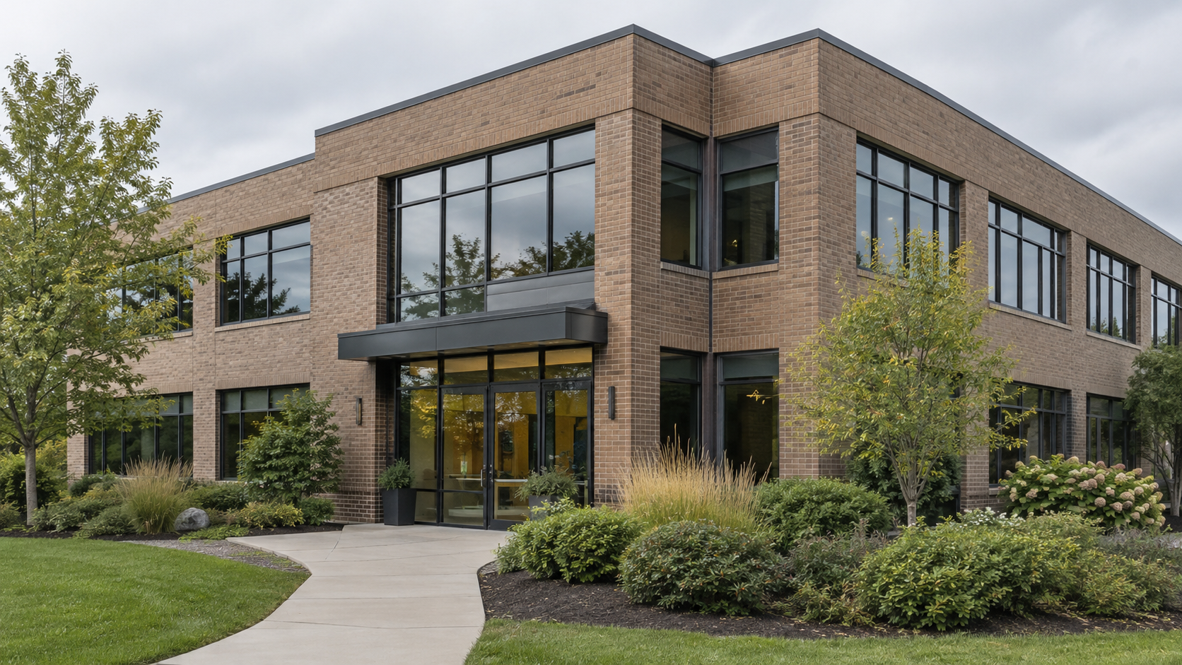 A two-story brick commercial building with a glass entrance, landscaped beds and a curved walkway.