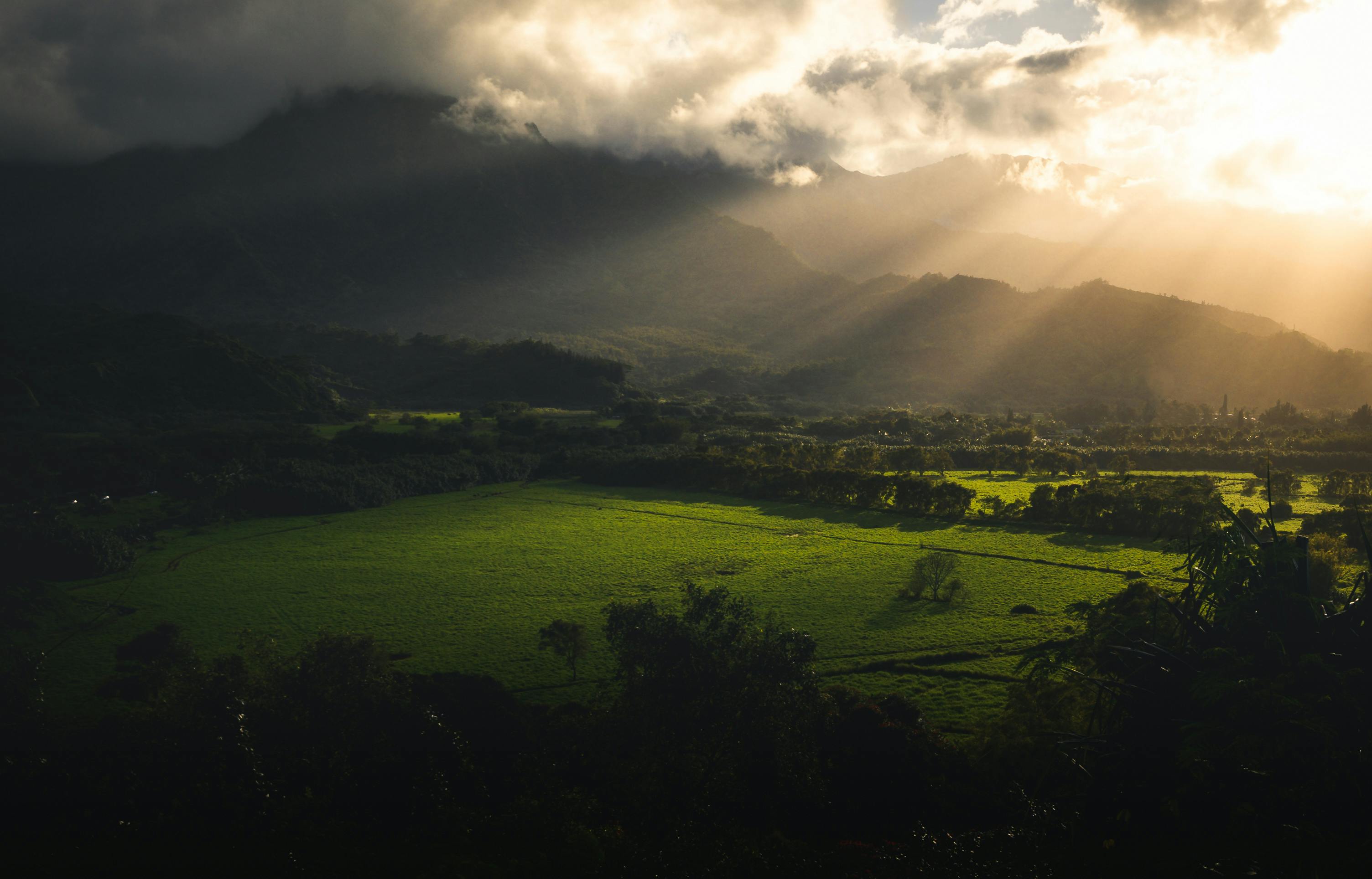 Sunlight breaking through clouds over a lush green Kauaʻi valley.