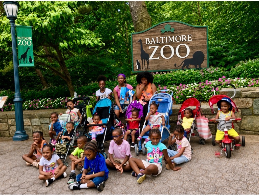 Baltimore Zoo Summer Field Trip Large group of Insight Kidz Care children and caregivers posing in front of the Baltimore Zoo entrance sign during a summer field trip