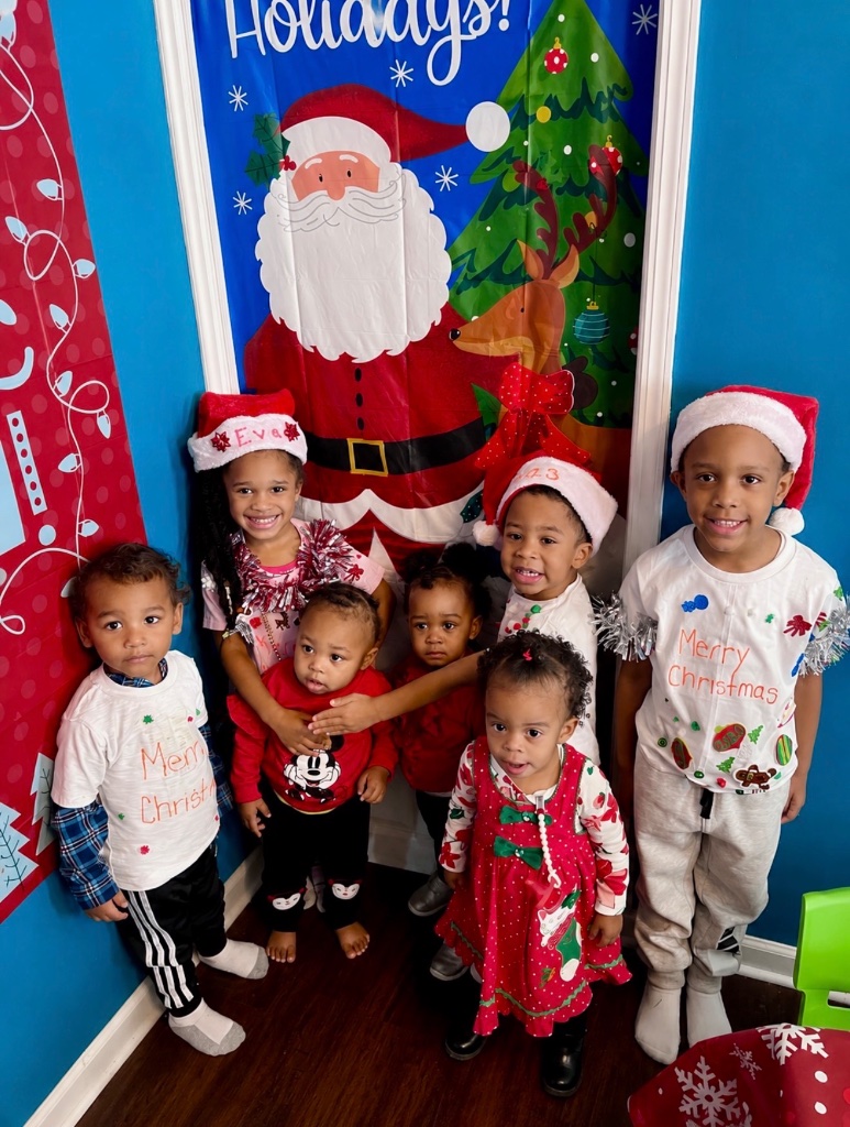 Christmas Holiday Photo Children wearing Christmas outfits and Santa hats posing in front of a holiday door banner at Insight Kidz Care in Baltimore