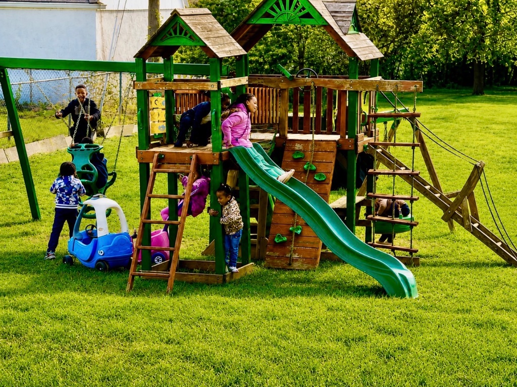Children playing on a large wooden swing set and slide in the fenced backyard at Insight Kidz Care licensed family child care in Baltimore
