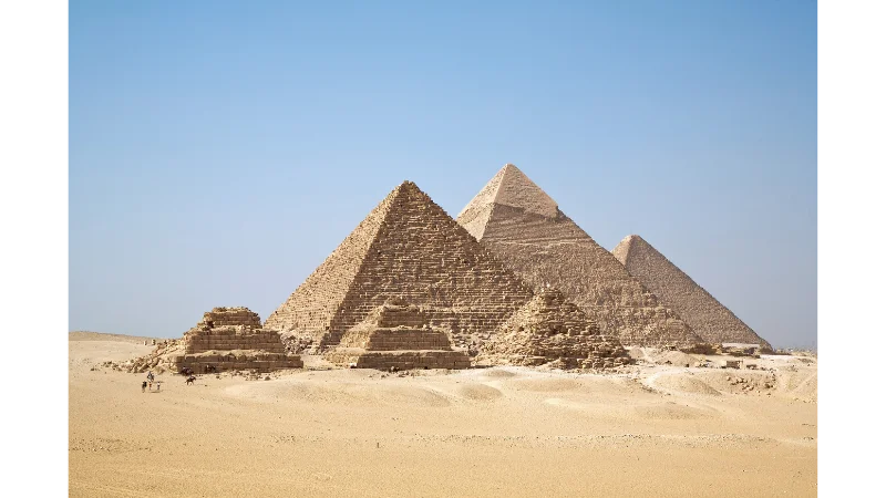 The three Great Pyramids of Giza rising from the desert under a clear blue sky.