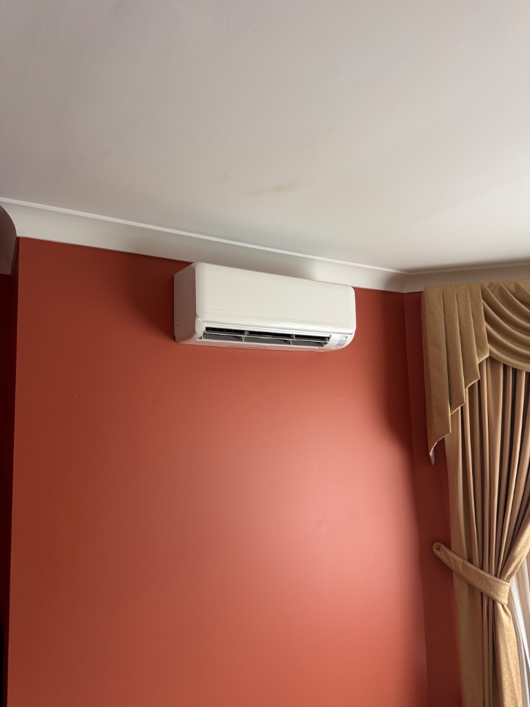 Split system indoor unit mounted on a terracotta feature wall with curtains in Leura