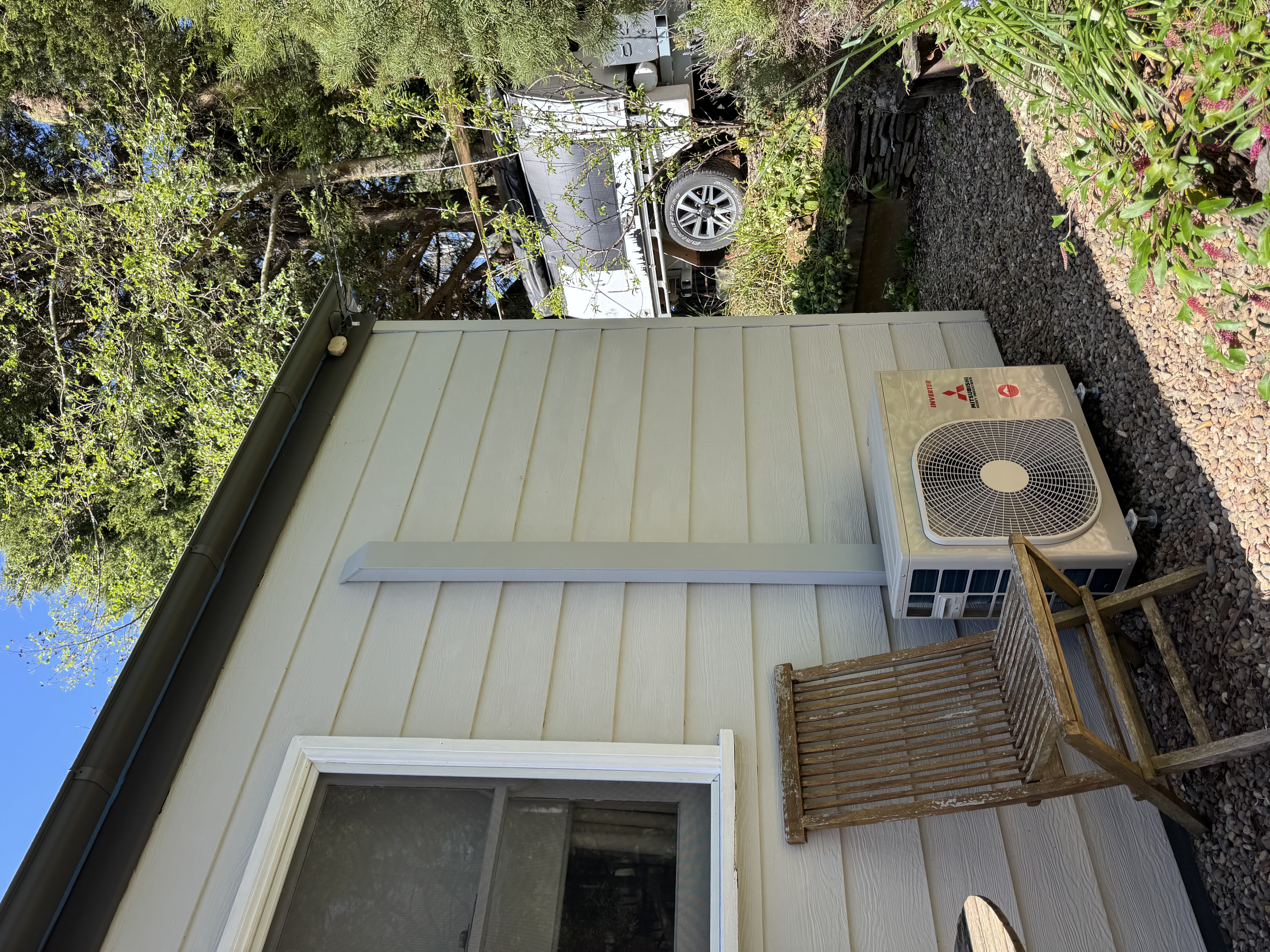 Outdoor air conditioning unit on gravel beside a weatherboard home