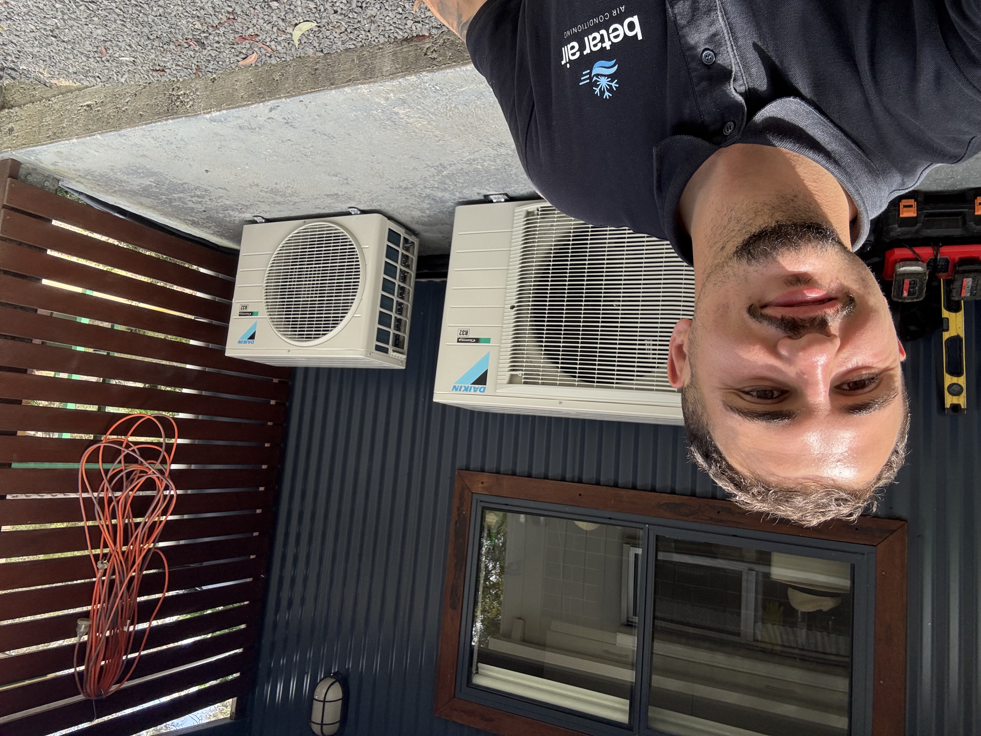 Person wearing a Betar Air polo beside the two Daikin outdoor units at the Mt Victoria project