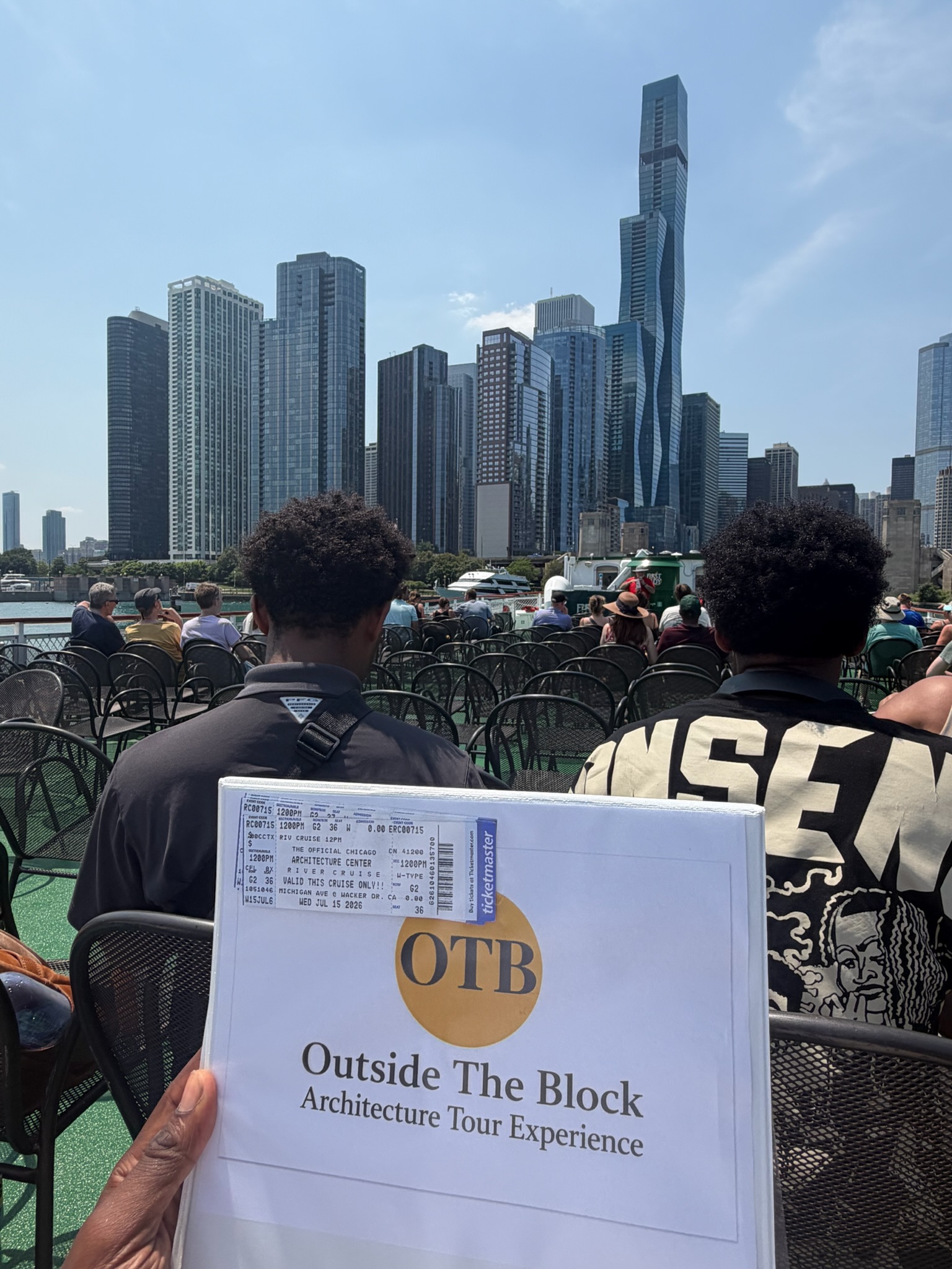 A student holding the Outside The Block Architecture Tour Experience sign with a Chicago Architecture Center river cruise ticket