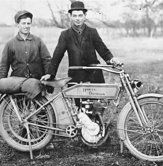 Black and white vintage photo of two men with an early Harley-Davidson motorcycle