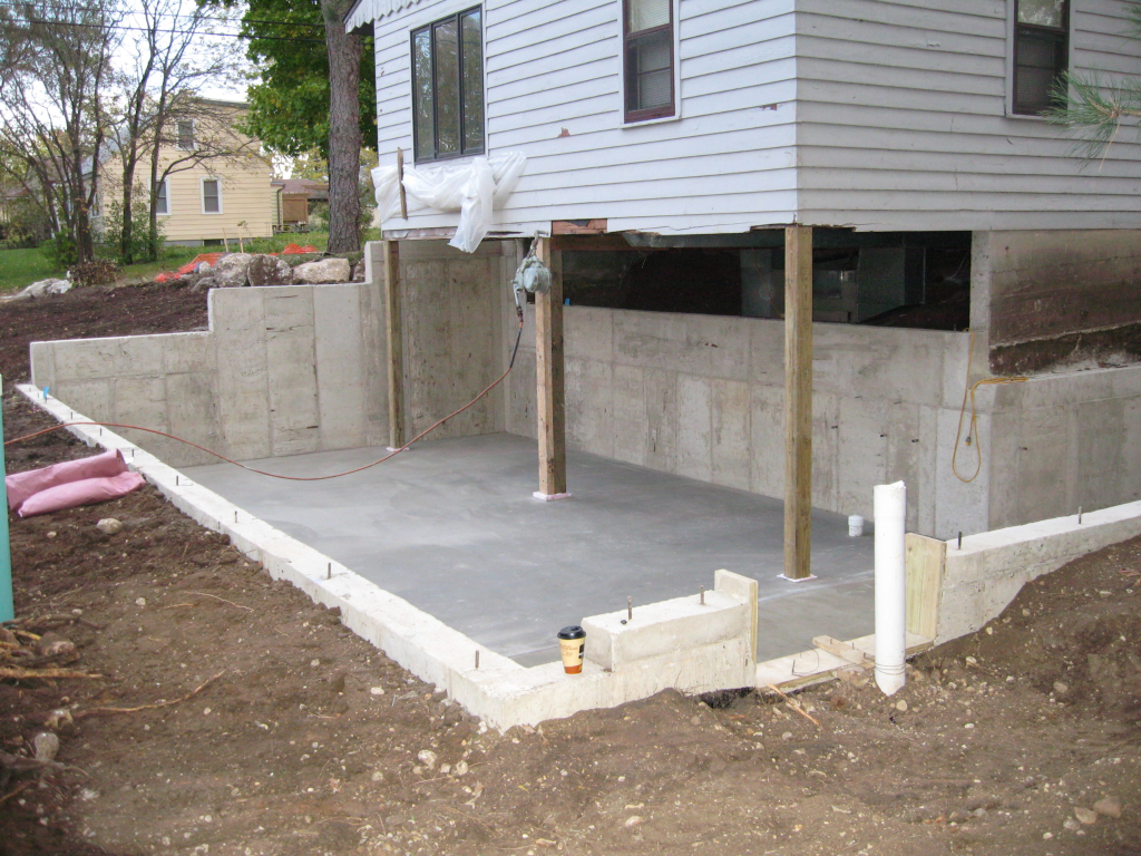 Addition foundation slab and poured concrete walls with support posts adjacent to existing house