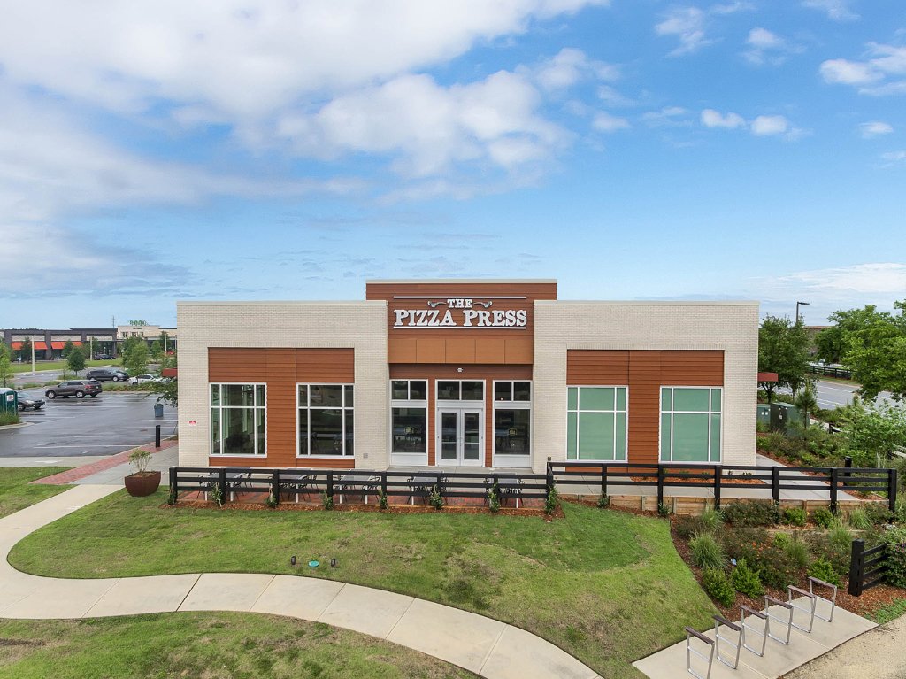 Exterior of The Pizza Press restaurant in Winter Garden, FL — stand-alone building with wood-composite siding, large glazing, and branded fascia signage