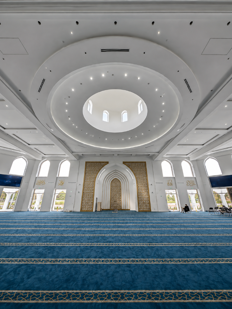 Interior of The Islamic Center of Orlando prayer hall with domed ceiling, gold mihrab, and teal prayer carpet