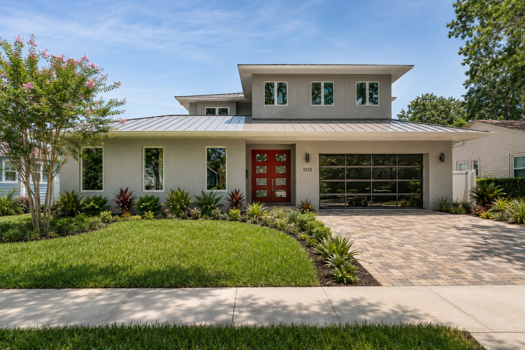 Contemporary spec home at 1332 W Yale Street, College Park, Orlando FL — gray stucco exterior with standing-seam metal roof, red double doors, glass garage, and tropical landscaping.