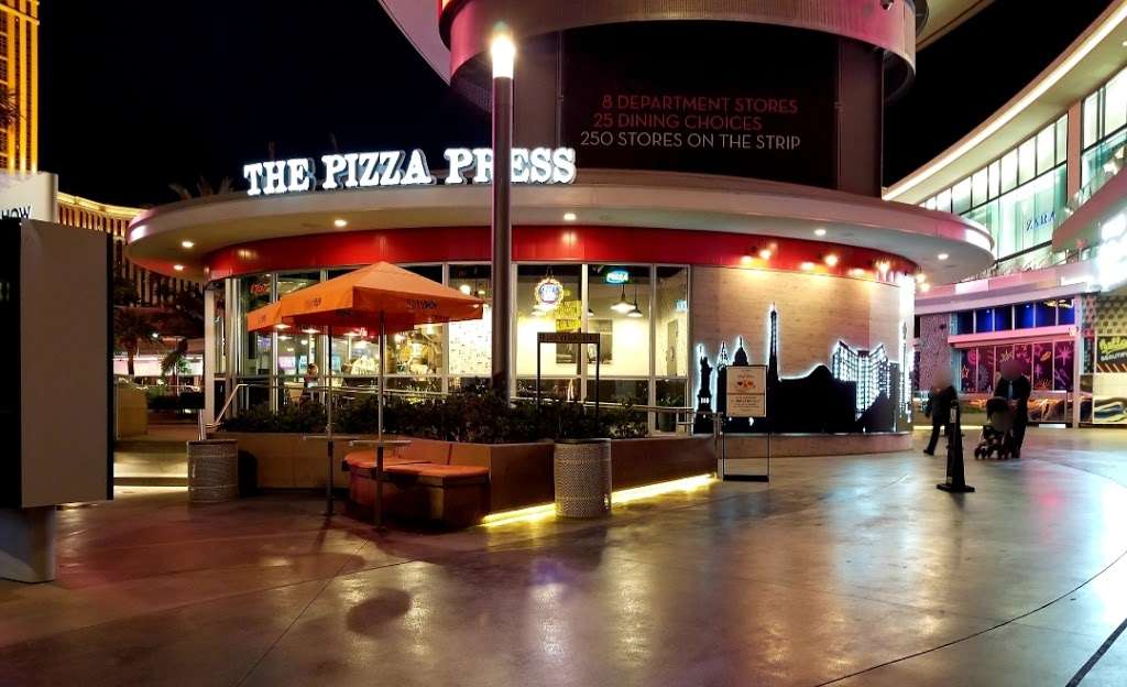 Exterior night view of The Pizza Press restaurant on the Las Vegas Strip with circular illuminated facade, neon signage, and outdoor seating
