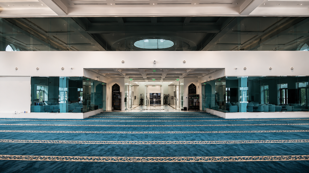 Interior of The Islamic Center of Orlando prayer hall with domed ceiling, gold mihrab, and teal prayer carpet