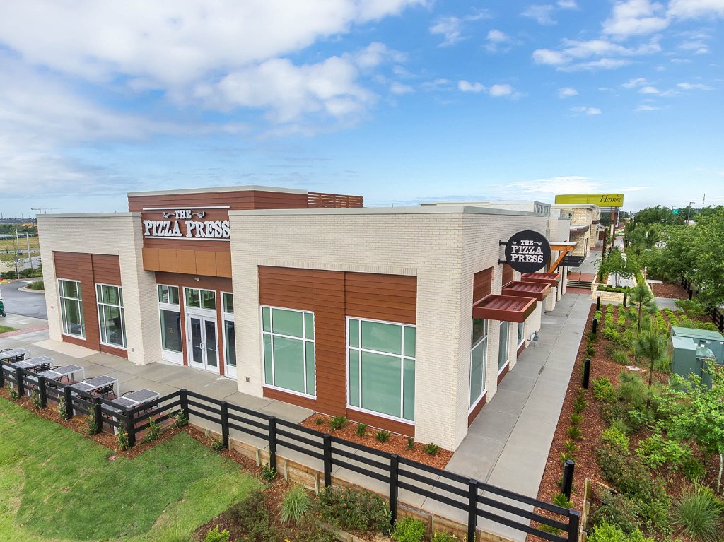 Exterior of The Pizza Press restaurant in Winter Garden, FL — stand-alone building with wood-composite siding, large glazing, and branded fascia signage