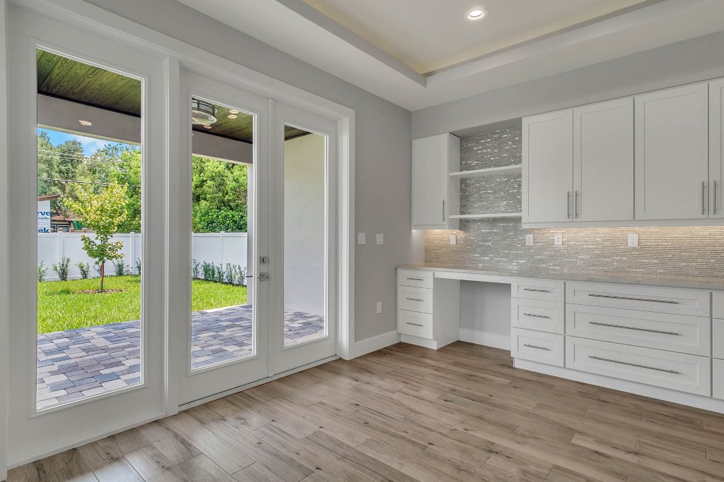 Contemporary spec home at 1332 W Yale Street, College Park, Orlando FL — gray stucco exterior with standing-seam metal roof, red double doors, glass garage, and tropical landscaping.
