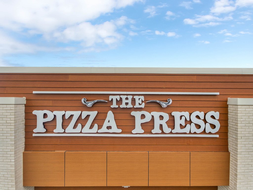 Exterior of The Pizza Press restaurant in Winter Garden, FL — stand-alone building with wood-composite siding, large glazing, and branded fascia signage