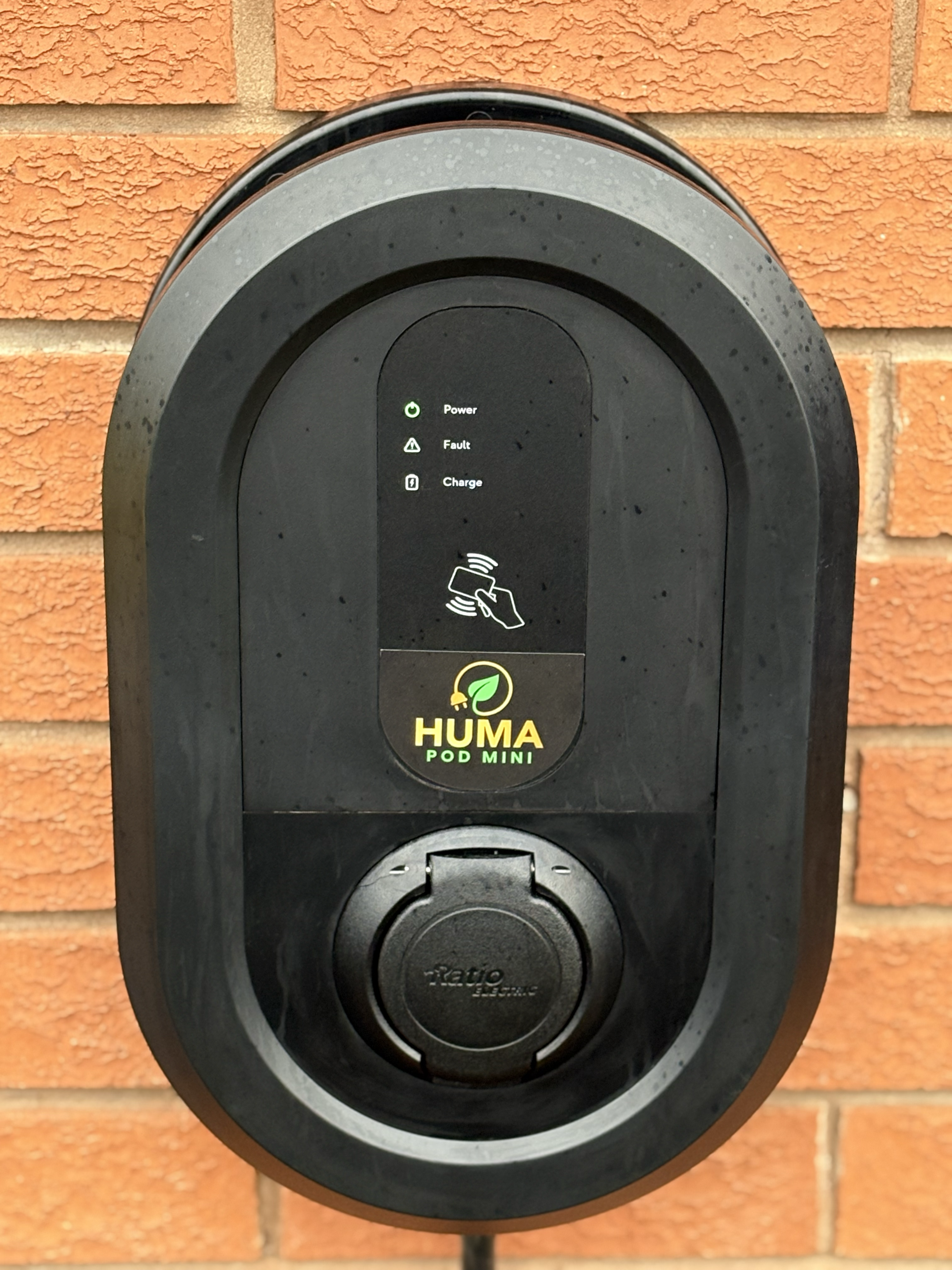 Close-up of the wall-mounted HUMA Pod Mini EV charger, showing its status indicators, HUMA Pod Mini branding and charging socket