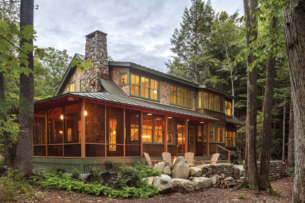 Glowing Maine lake house at dusk with screened porch and Adirondack chairs