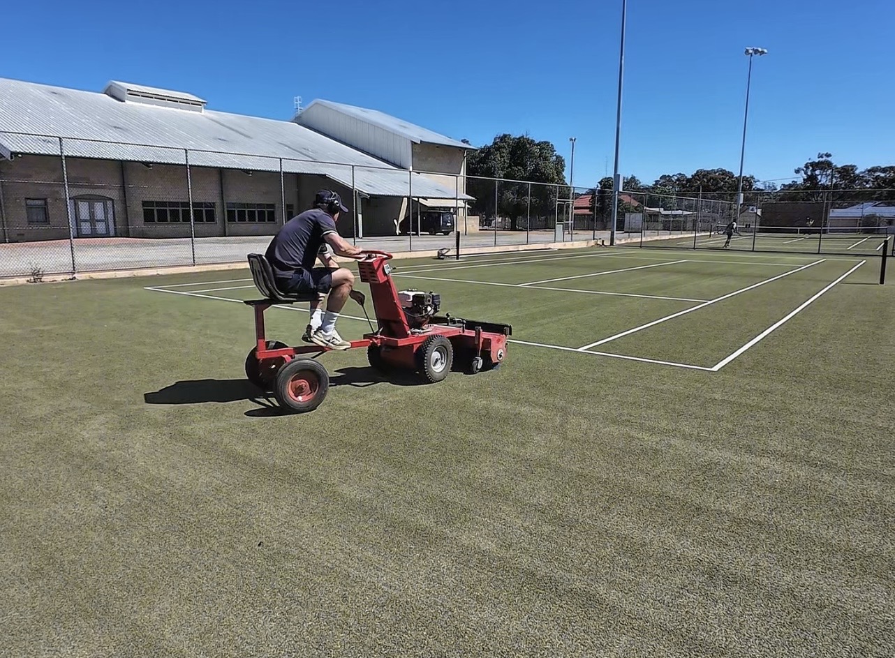 Ride-on grooming machine servicing a synthetic grass tennis court