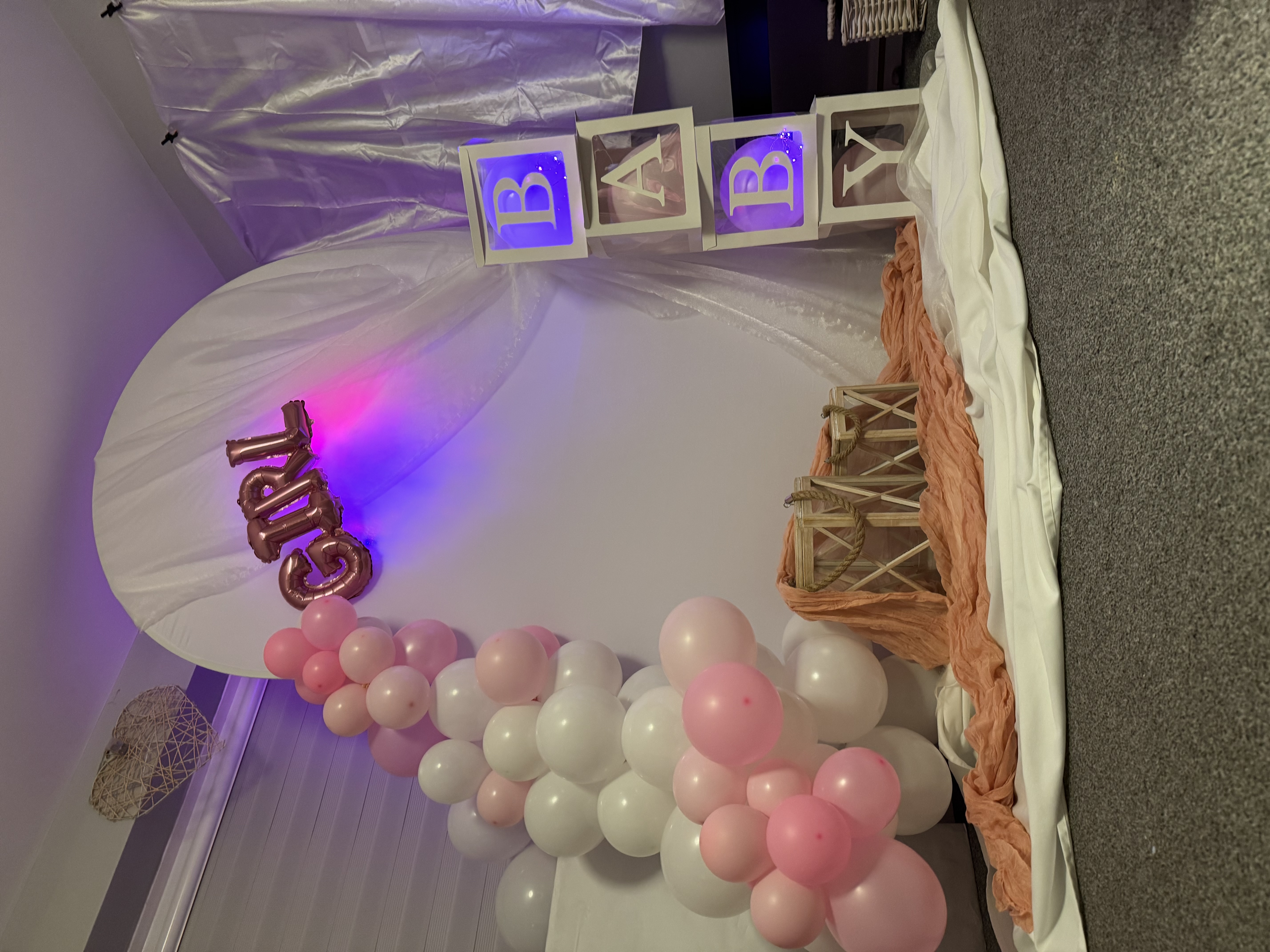 Girl baby shower setup with floral arch, balloon garland and illuminated BABY letter blocks