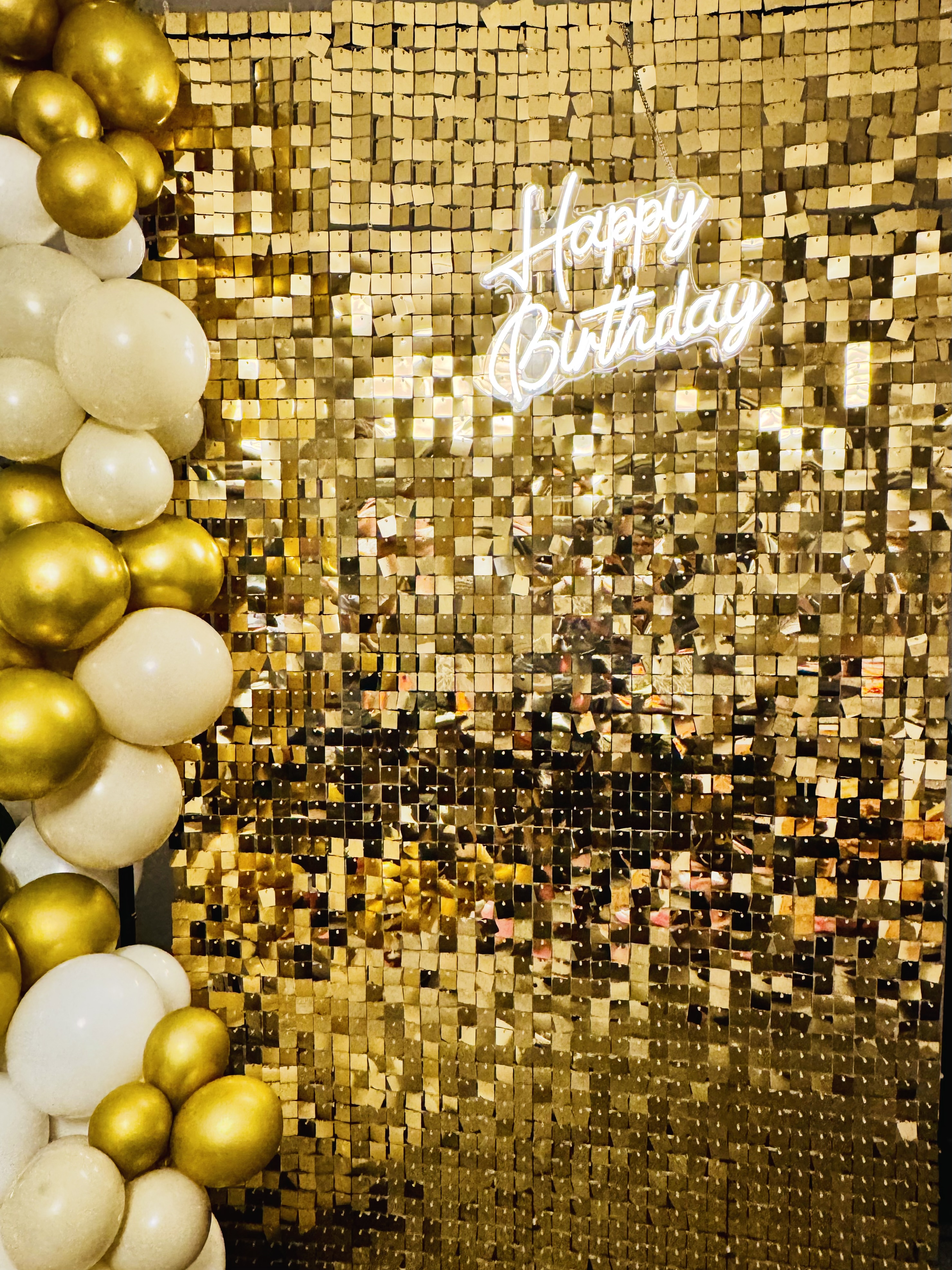 Happy Birthday gold sequin backdrop with white and gold balloon garland and neon sign