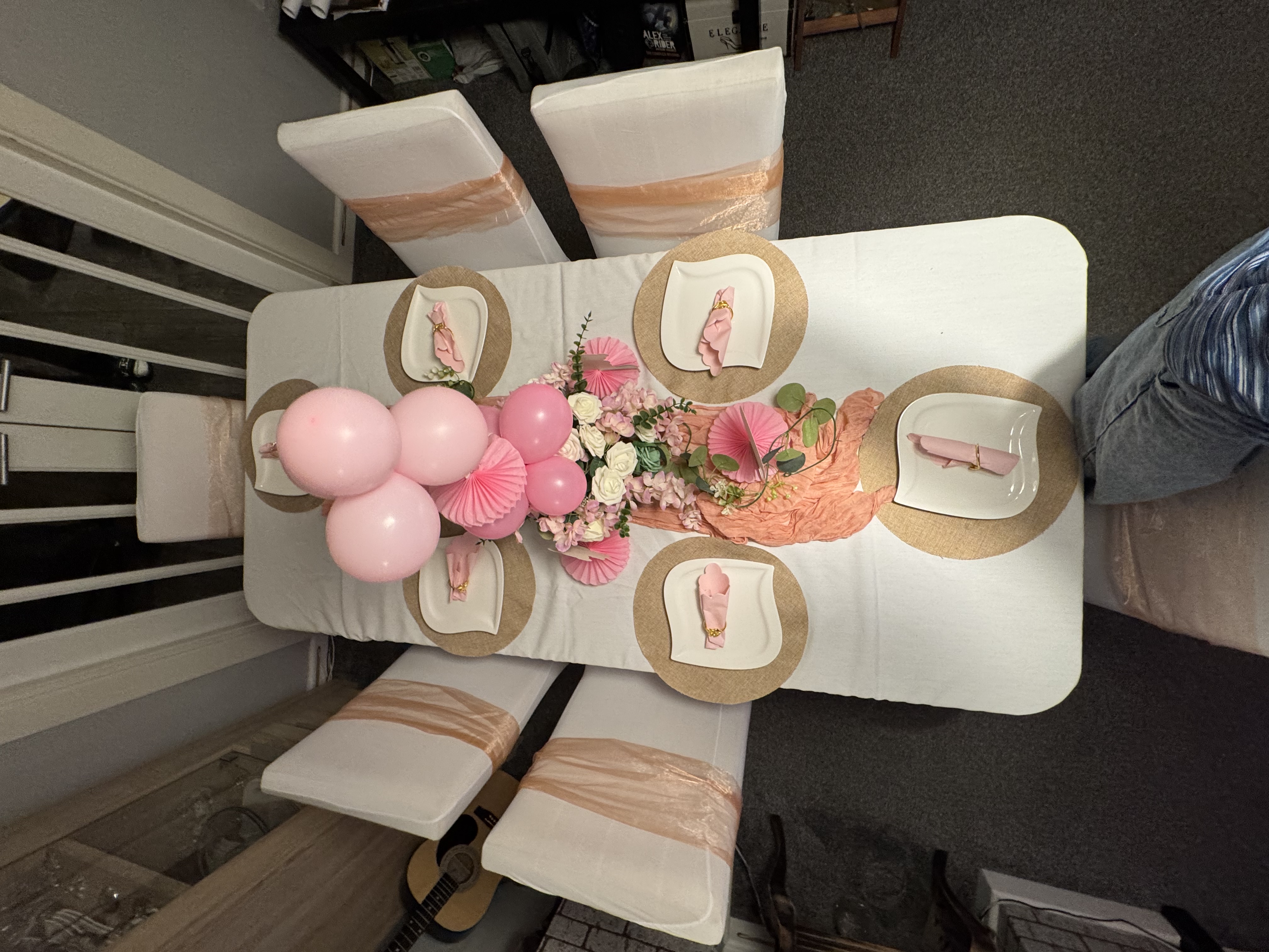 Overhead view of pink themed table setting with floral runner, balloon accents and woven placemats