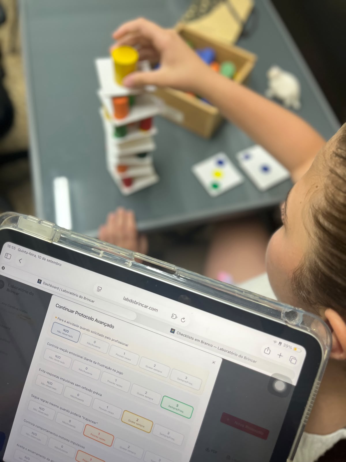 Profissional acompanhando o Protocolo Avançado no tablet durante uma sessão de brincar com peças coloridas