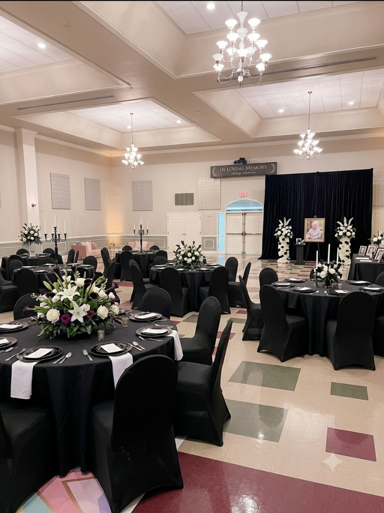 Schwenkfeld Hall banquet space configured for a memorial service with black linens, floral centerpieces, and a portrait memorial backdrop