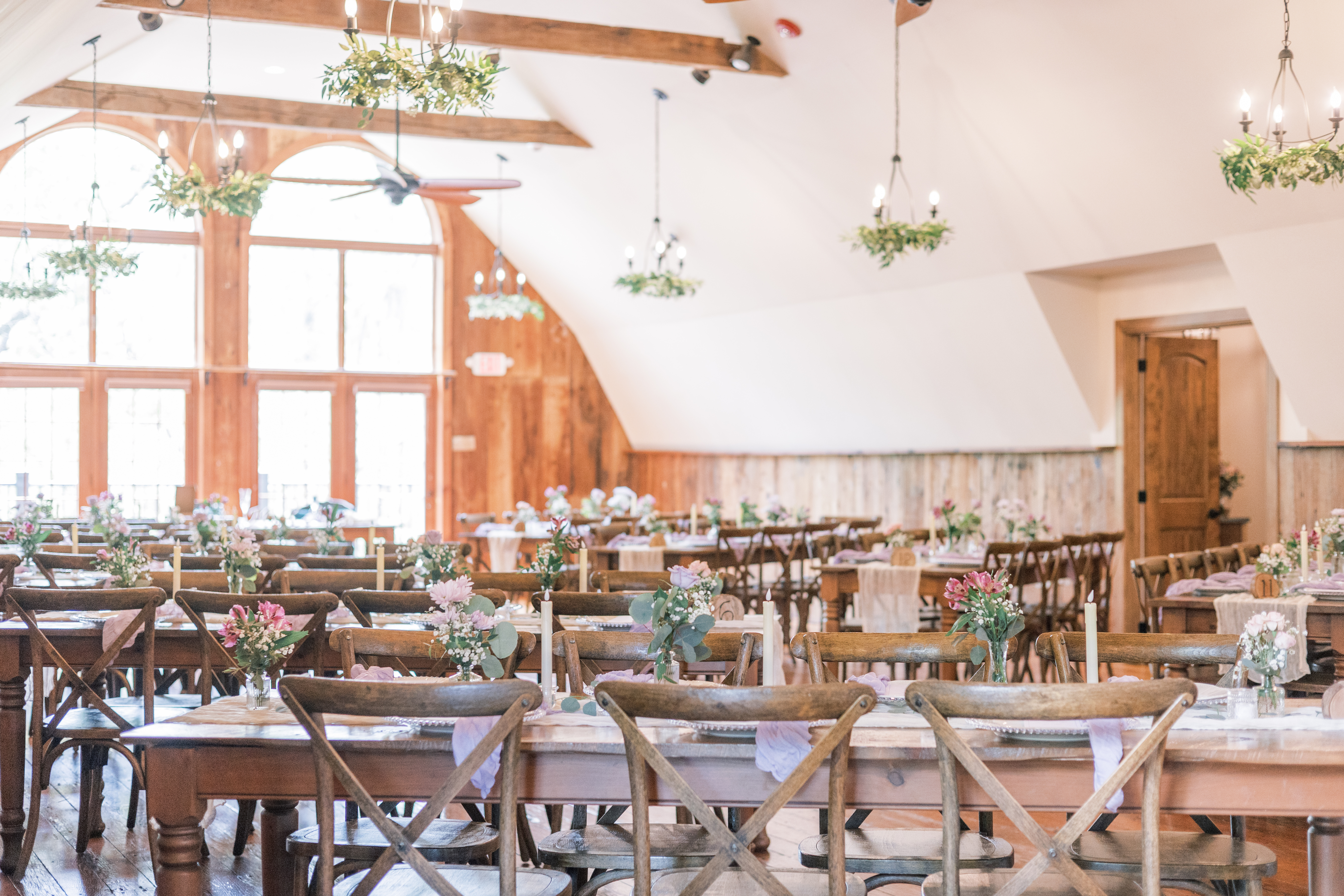 Historic Stonebrook barn reception interior in Perkasie PA with wooden farm tables, floral chandeliers and arched windows