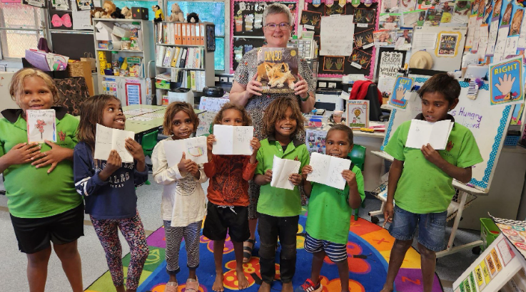Teacher reading to a group of students holding their work