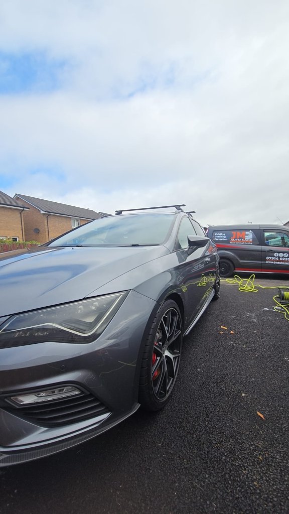 Charcoal grey hatchback parked next to the JM Auto Care van on site