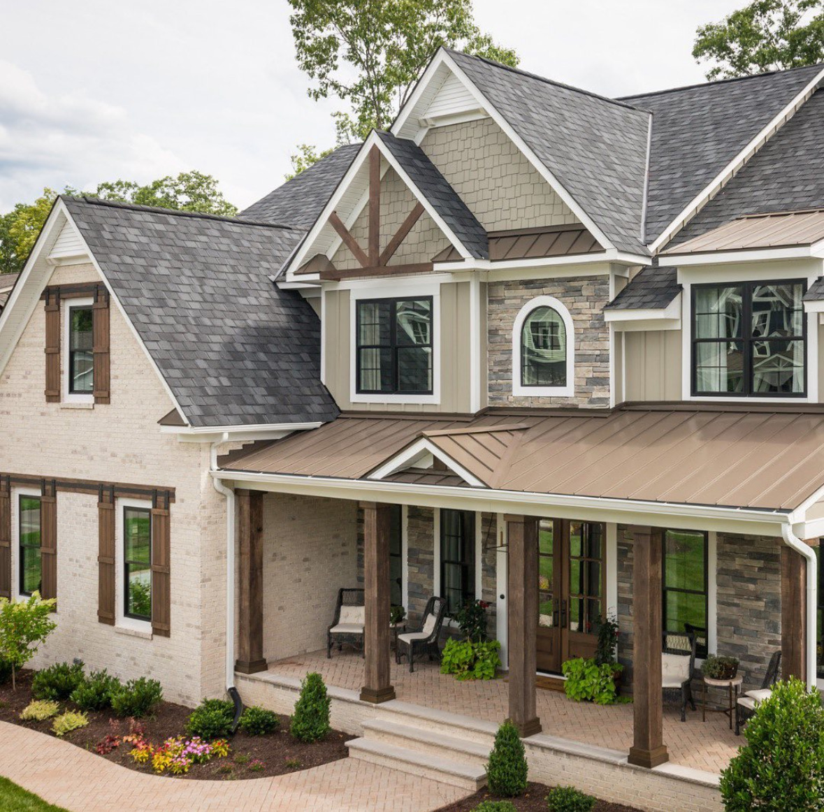 High-end multi-story home with dark gray architectural shingles, bronze standing seam metal porch roof, board-and-batten siding, and natural stone veneer