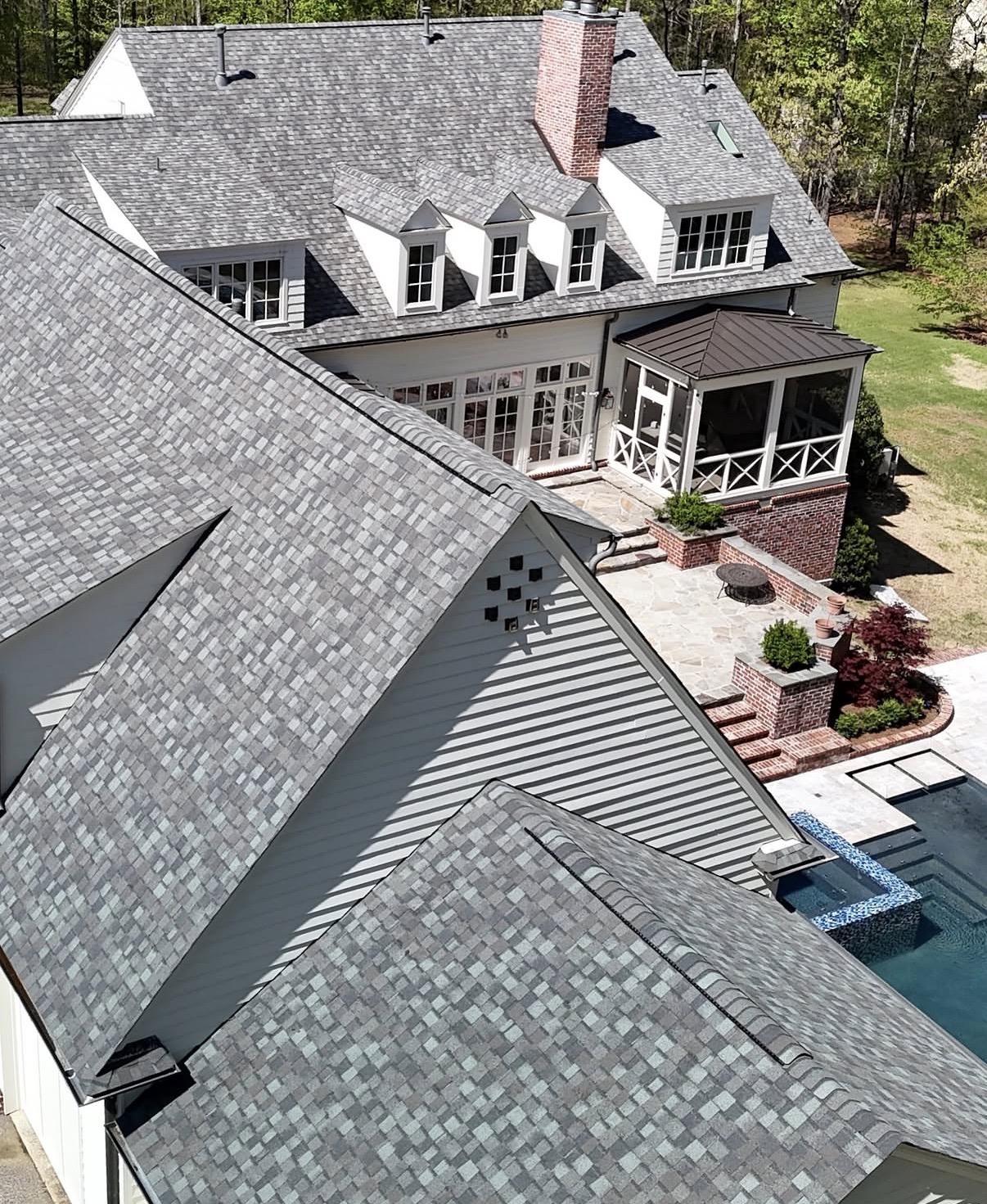 Rear elevation of large home with newly installed architectural asphalt shingle roof overlooking stone patio and swimming pool