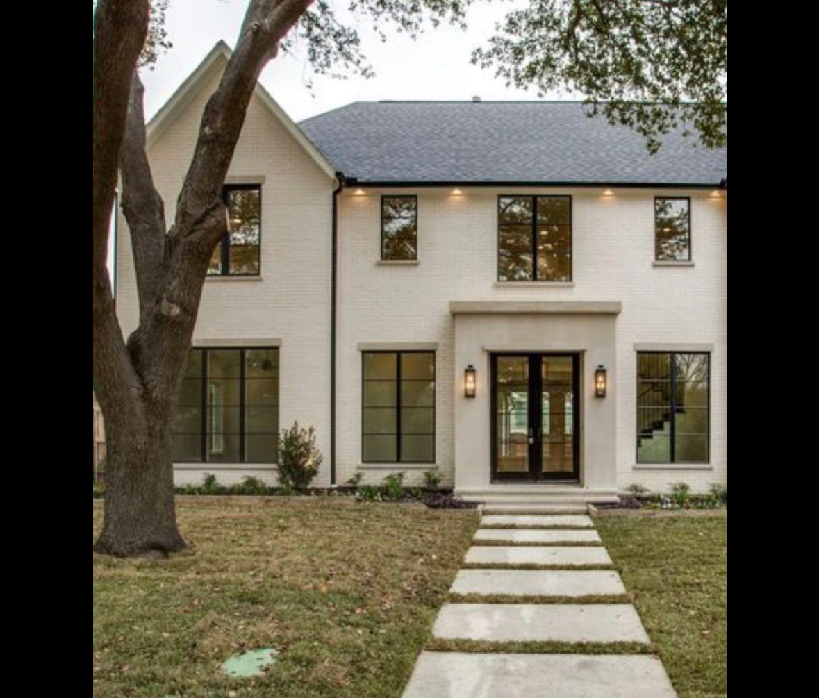 Two-story white painted brick home with dark charcoal architectural asphalt shingle roof and stone entry surround