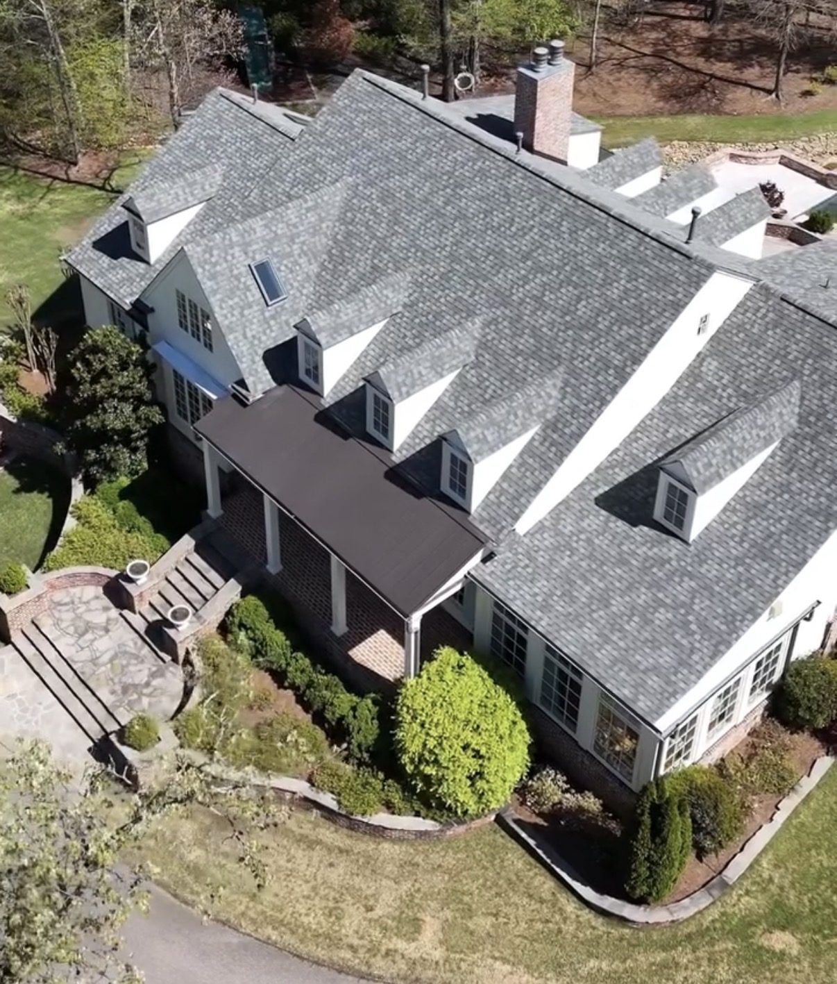 High-angle view of two-story home with charcoal-grey asphalt shingle roof, white siding, and brick masonry lower level