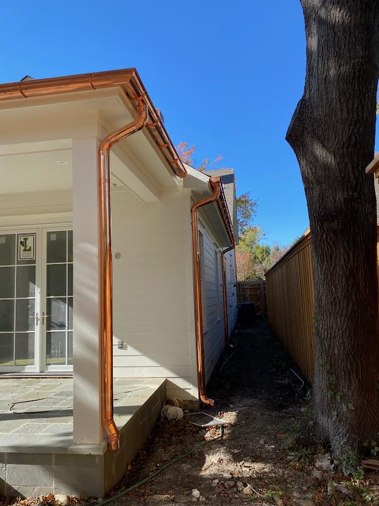Close-up of newly installed polished copper gutters and downspouts on a white siding home with covered porch