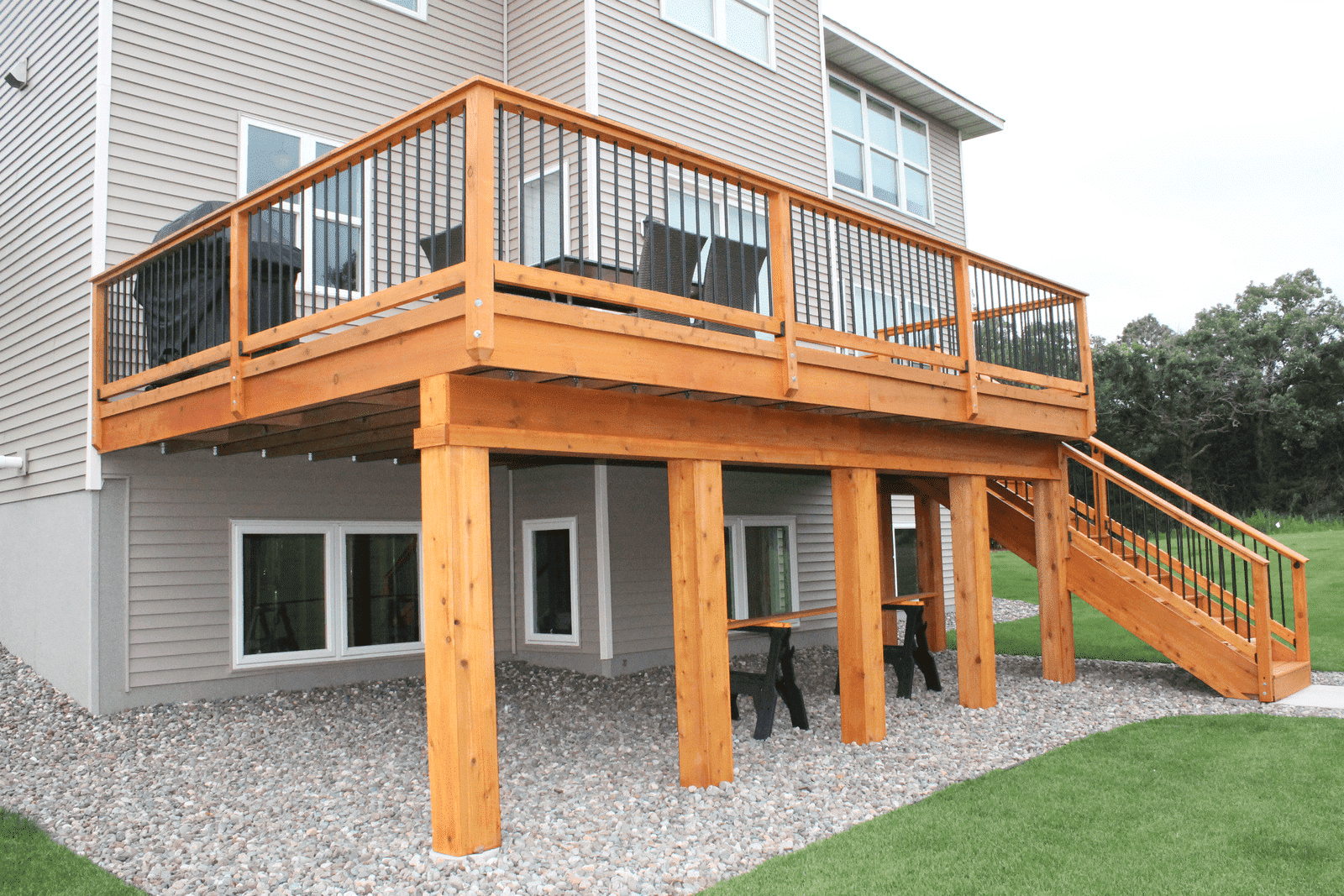 Newly constructed raised cedar wood deck with black metal baluster railings and river rock foundation
