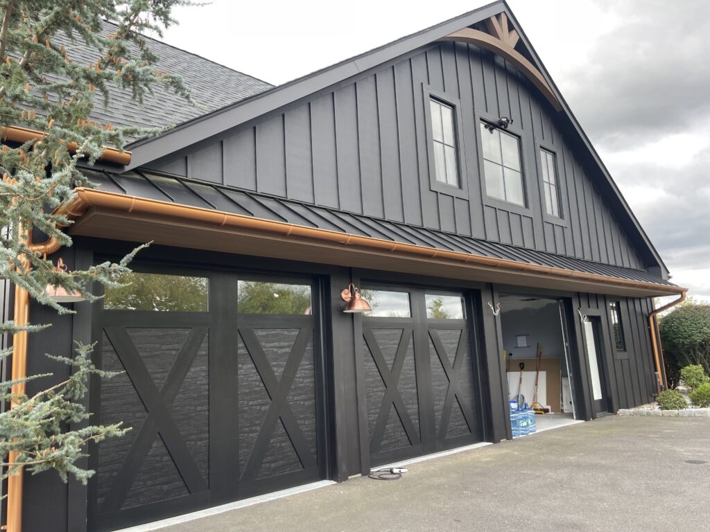 Modern dark board-and-batten garage with standing seam metal roof, copper gutters, and carriage house style garage doors