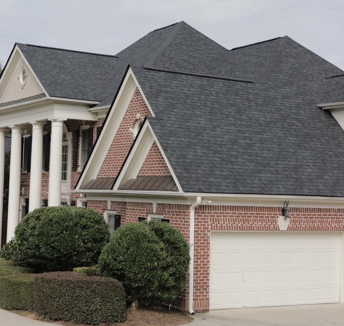 Red brick two-story home with white portico columns and dark charcoal architectural asphalt shingle roof replacement